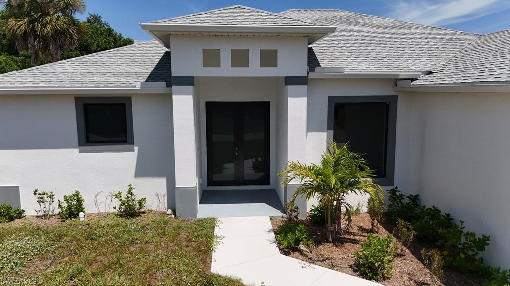 Contemporary stucco exterior featuring a dual-door entryway, architectural window framing, and a light gray shingle roof