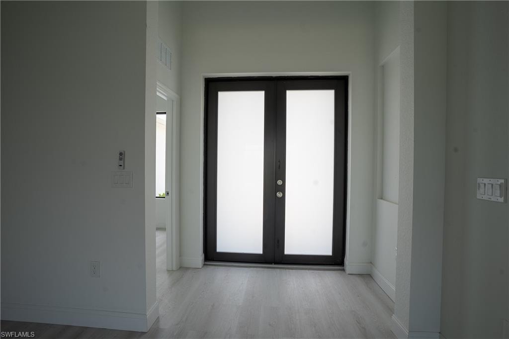 Double entry doors featuring frosted glass panels and dark frames, complemented by light wood-finish flooring