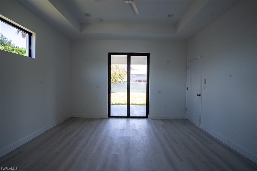 Spacious room featuring light wood-finish flooring, a tray ceiling with recessed lighting and a ceiling fan, and white walls