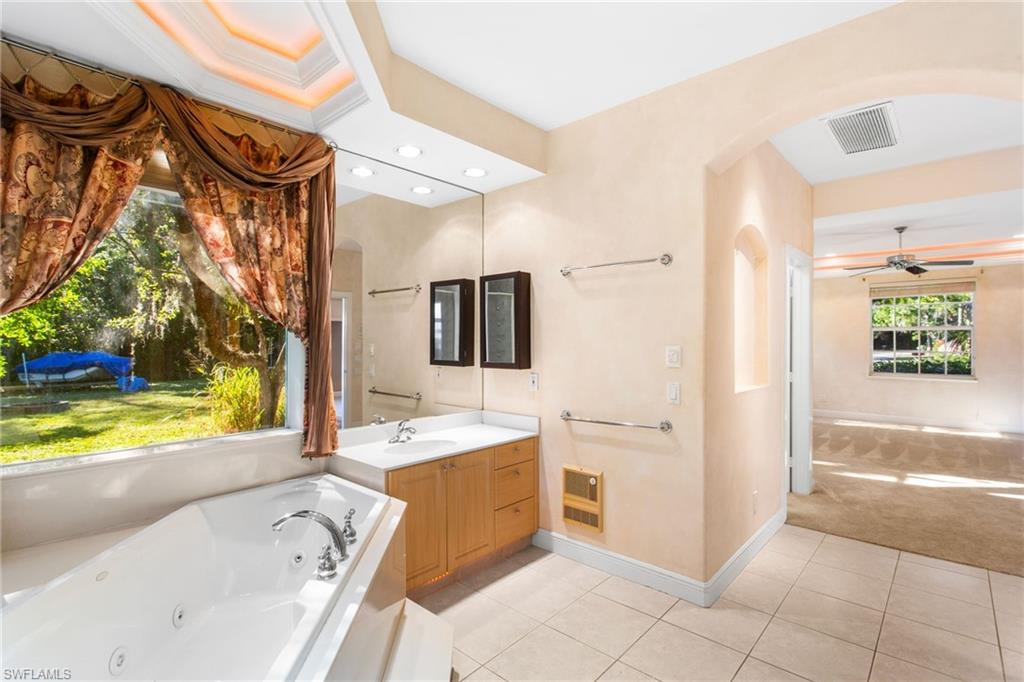 Spacious bathroom featuring a built-in jetted tub, expansive vanity with dual sinks, large mirror, and tiled flooring