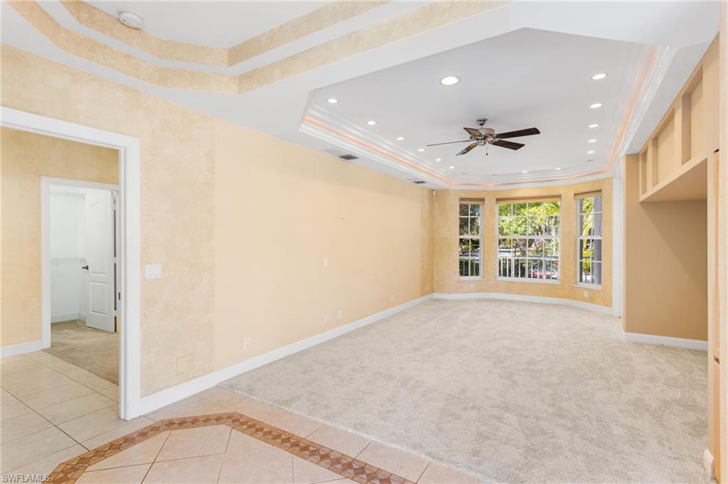 Spacious room with a tiered tray ceiling featuring recessed lighting and a ceiling fan