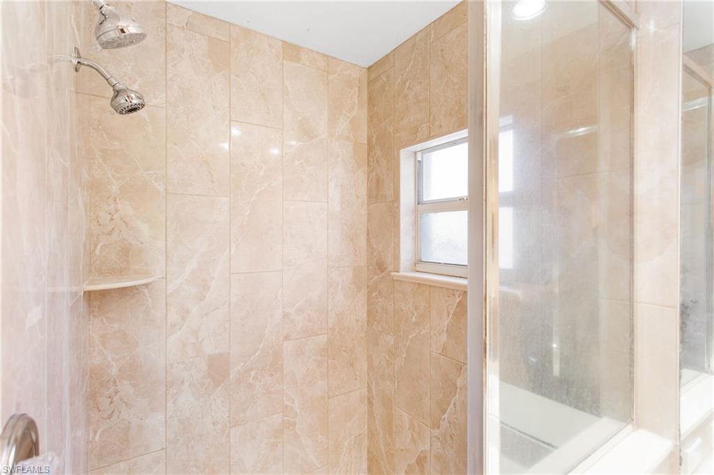 Shower with light-toned tiled walls, dual showerheads, and a built-in corner shelf