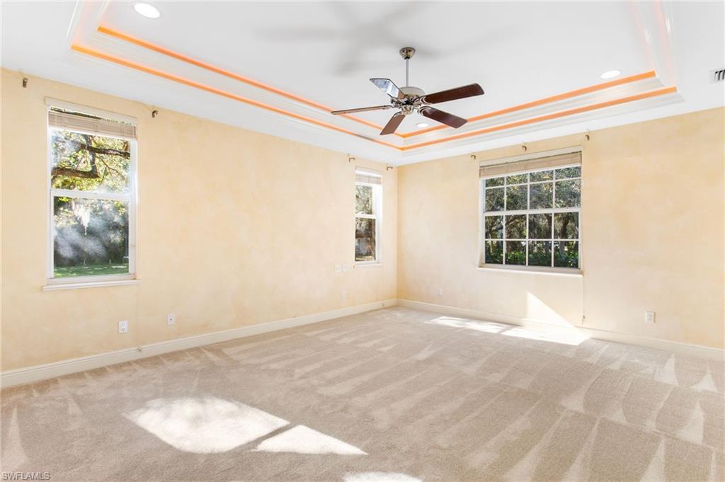 Room featuring a tray ceiling with recessed lighting and accent trim, a ceiling fan, light-toned carpet flooring, and multiple windows with blinds