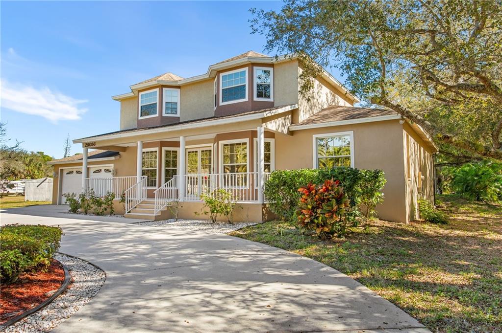 Two-story stucco residence featuring a covered front porch with white railings, a wide concrete driveway, and established landscaping