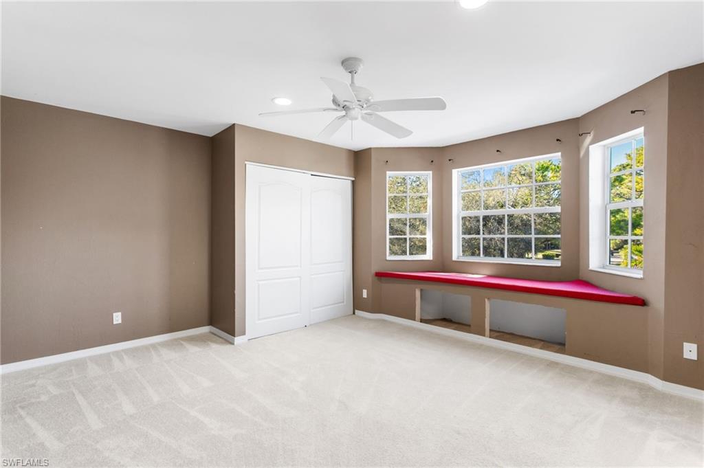 Spacious room featuring a bay window with a built-in bench, neutral carpeting, a ceiling fan, and bi-fold closet doors