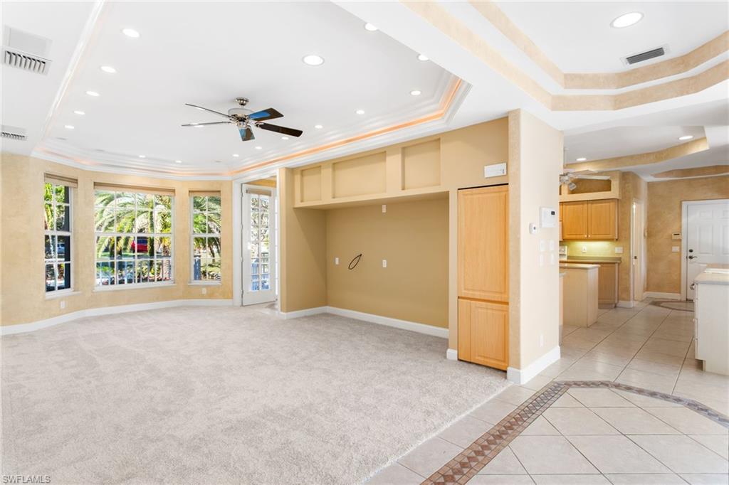 Spacious carpeted room featuring a bay window, recessed lighting, ceiling fan, and tray ceilings