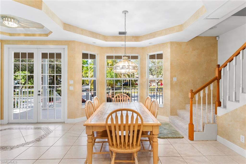 Dining space featuring bay windows, tray ceiling, tile flooring with decorative inlay, and double French doors opening to a porch