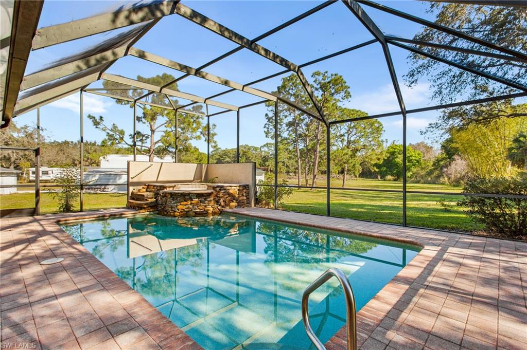 Screened swimming pool enclosure featuring a rectangular pool with integrated spa, stone-clad accent wall, and paver decking
