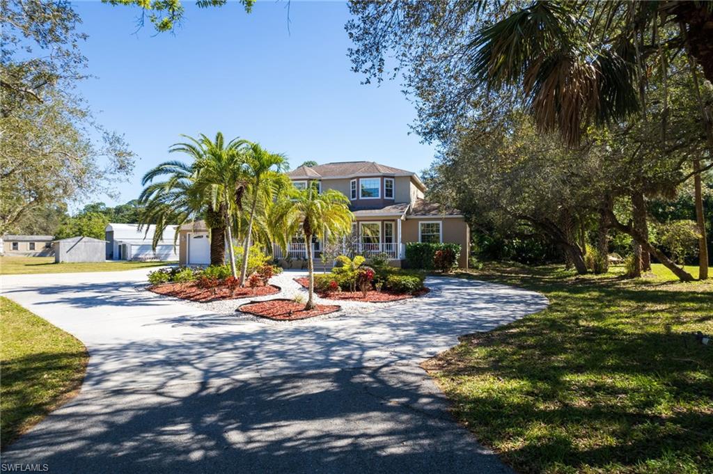 Two-story residence featuring a large paved driveway, mature palm trees, and established landscaping