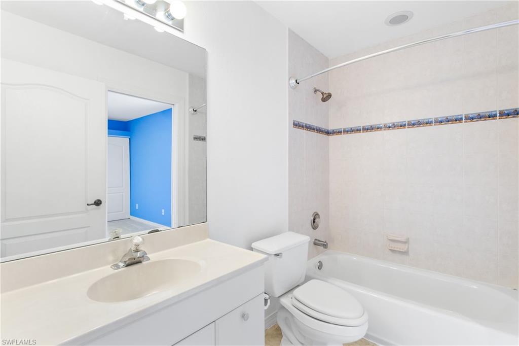 Full bathroom featuring a single vanity with an integrated sink, a large mirror, and a tub/shower combination with tiled walls and a decorative border
