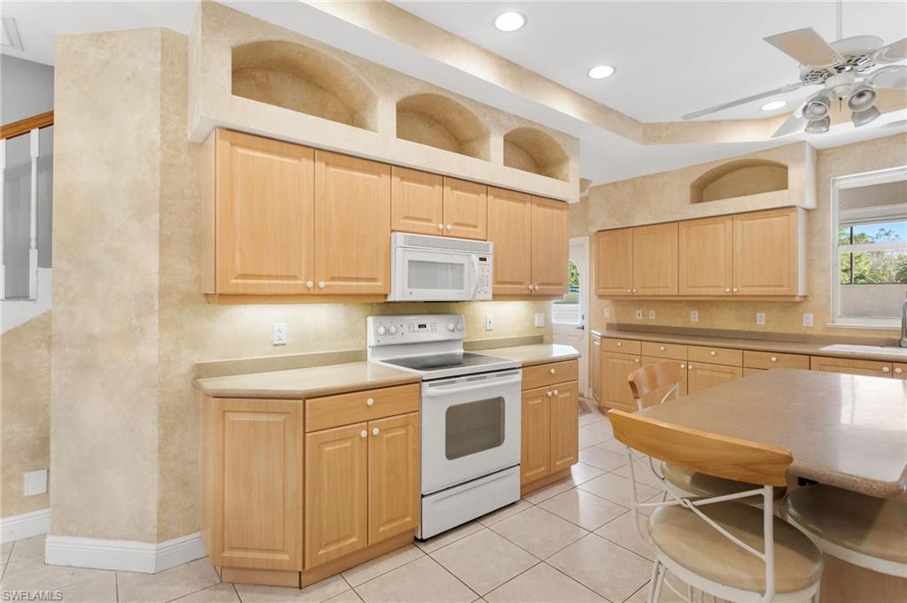 Kitchen featuring abundant light wood cabinetry, white appliances, tiled flooring, recessed lighting, and built-in display arches