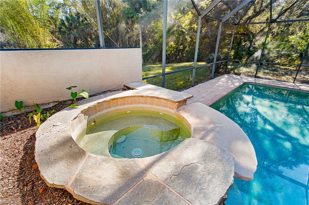 In-ground spa with natural stone coping and a brick-finish surround, accompanied by a screened enclosure and an adjacent swimming pool with a brick paver deck