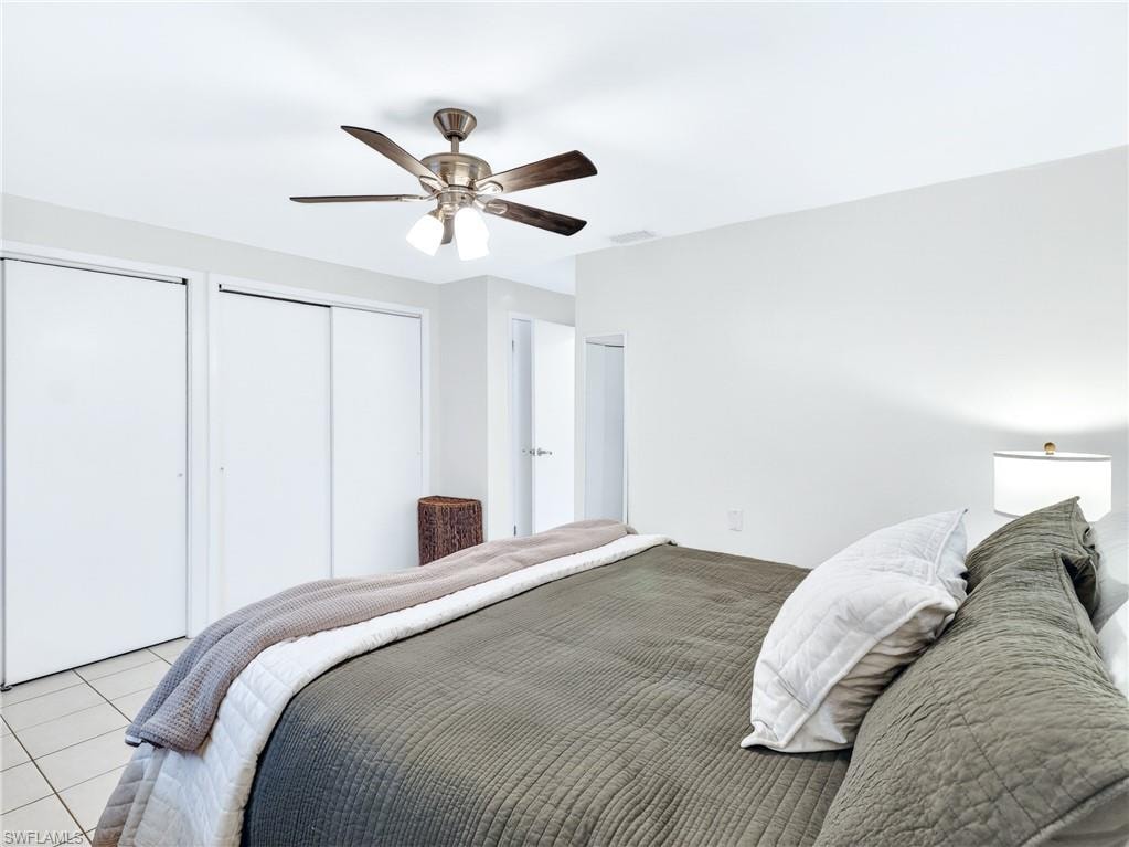 Spacious bedroom with white walls, ceiling fan with light fixture, and tile flooring