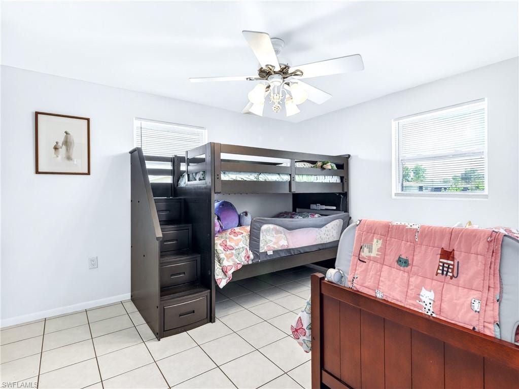 Bright room featuring white walls, tile flooring, a ceiling fan with light, and two windows with blinds