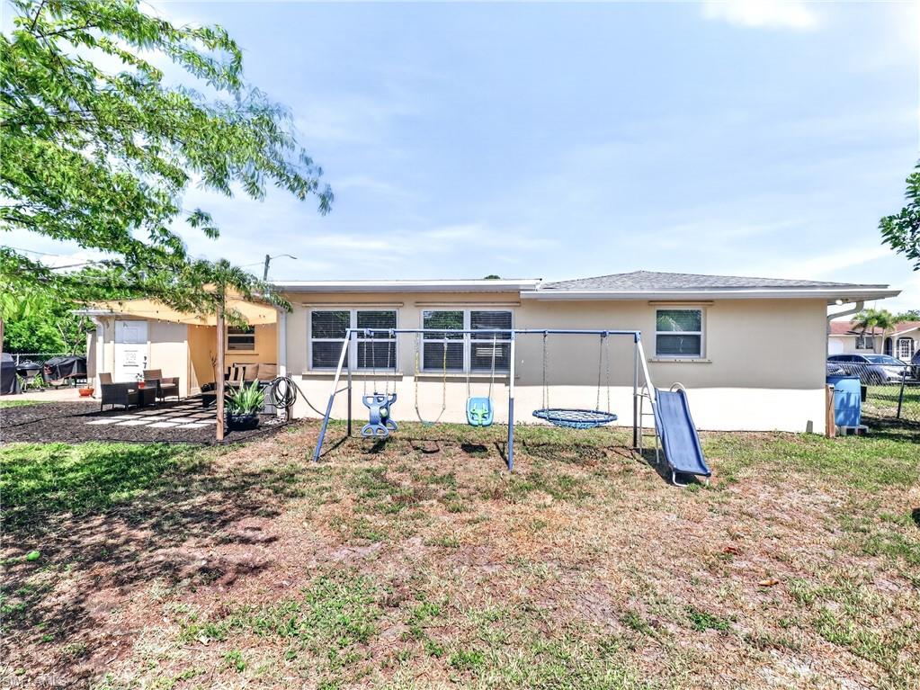 Expansive rear yard featuring a paved patio area with a sun shade, multiple windows, and a stucco exterior