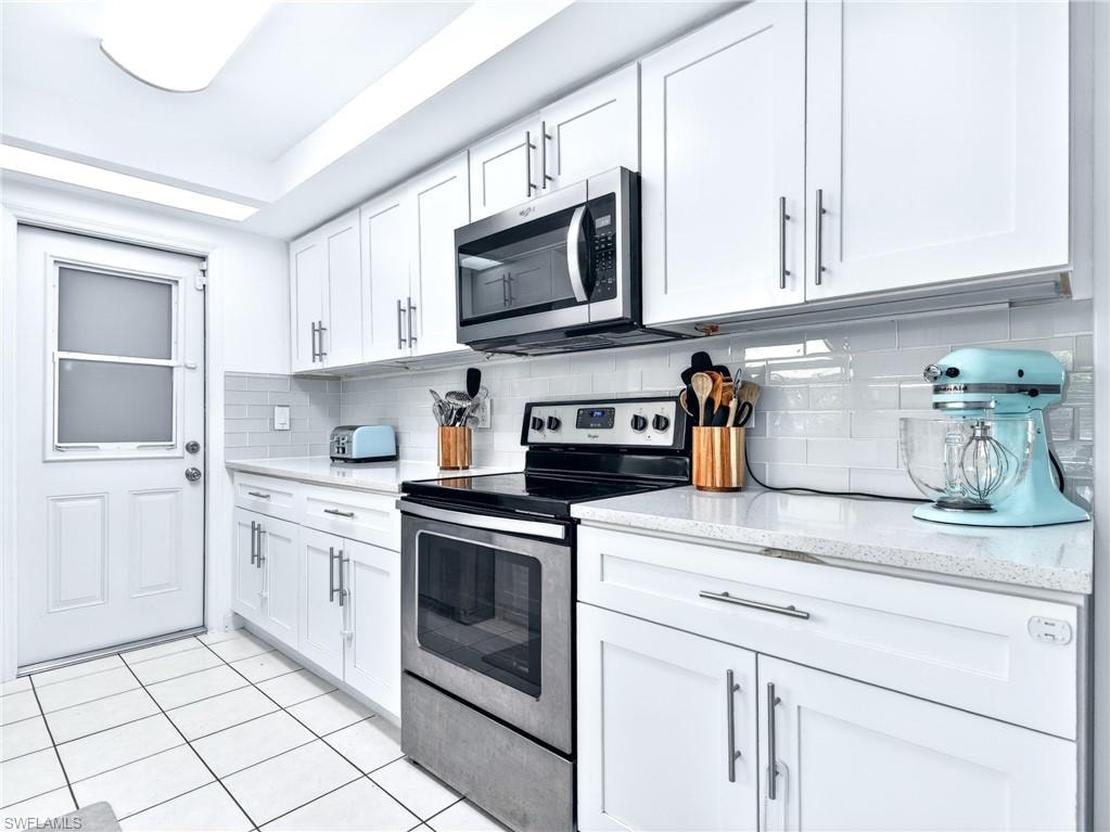 White kitchen featuring a stainless steel range and microwave, subway tile backsplash, white shaker-style cabinetry, and light-toned countertops