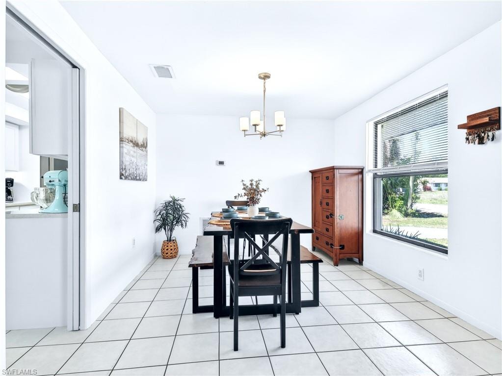 Bright dining area featuring a modern chandelier, a large window with blinds, and tile flooring