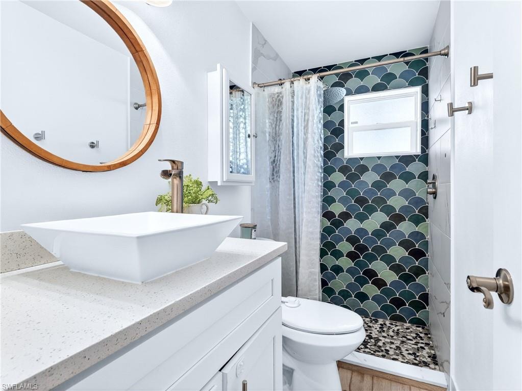 Contemporary bathroom featuring a vessel sink with a bronze-finish faucet, a wood-framed mirror, white cabinetry, and a shower with scallop-patterned tile, a privacy window, and pebble-finish flooring