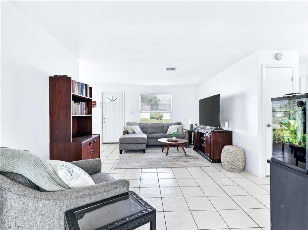 Bright living area featuring white tile flooring, a white paneled entry door with decorative glass, and a window with blinds