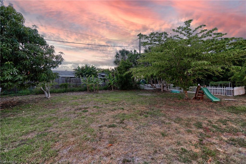 Spacious backyard featuring mature trees, a privacy fence, a white picket fence, and a green slide