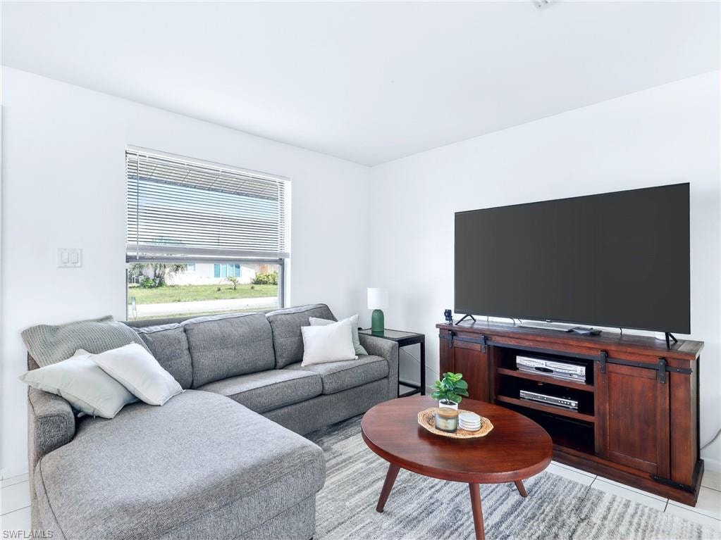 Living area featuring white tile flooring, a large window with horizontal blinds, and clean white walls