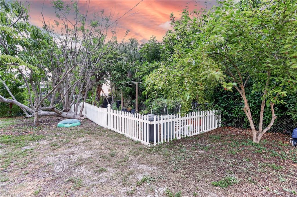 Fenced property area featuring a white picket fence, mature trees, and a partially visible chain-link fence