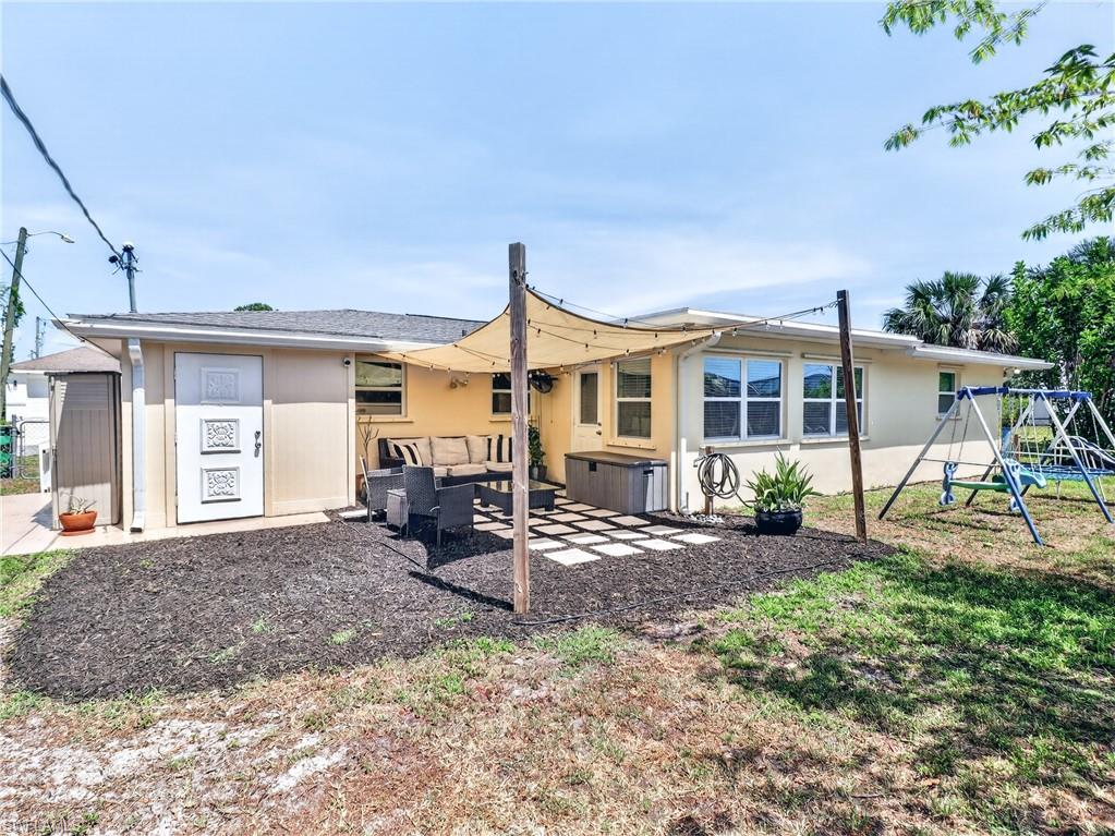 Rear exterior featuring a patio with shade sail, exterior storage shed, multiple windows, and a landscaped area with dark mulch