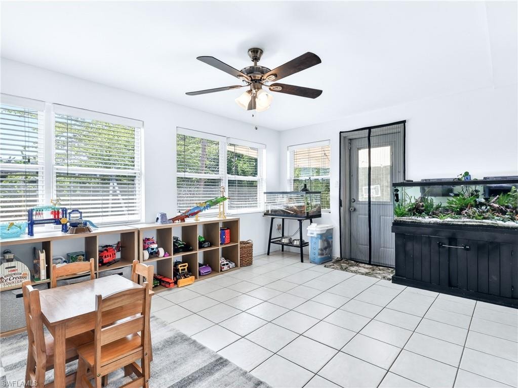 Bright room featuring white tile flooring, multiple windows with horizontal blinds, a ceiling fan with light fixture, and a rear door with a screen