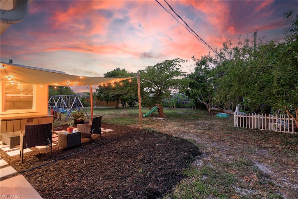 Expansive backyard featuring a shaded patio area, manicured garden beds with dark mulch, and mature trees