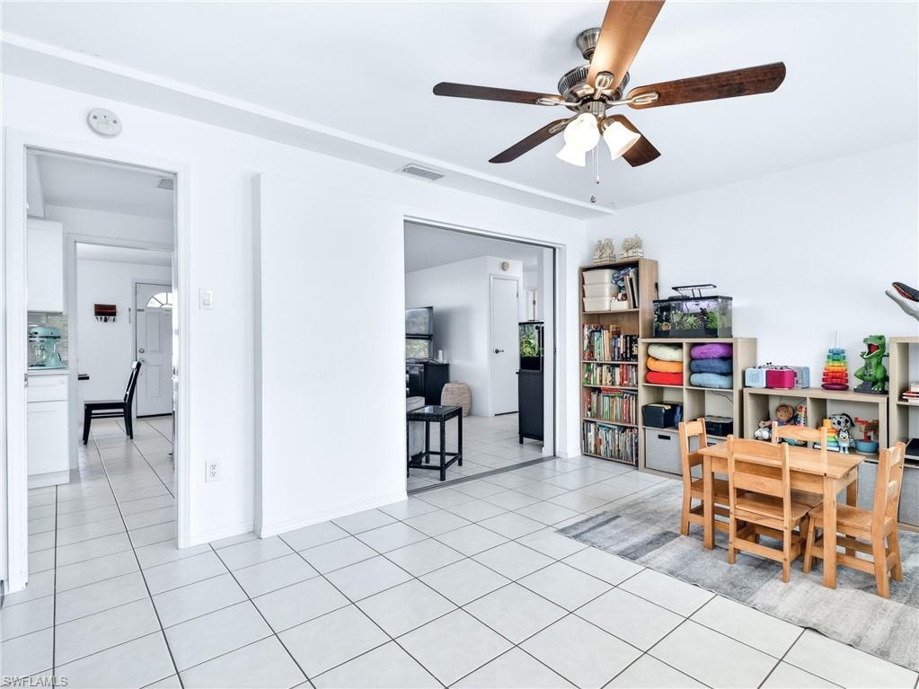 Bright room featuring tile flooring, a ceiling fan with light fixture, and an open doorway to an additional space