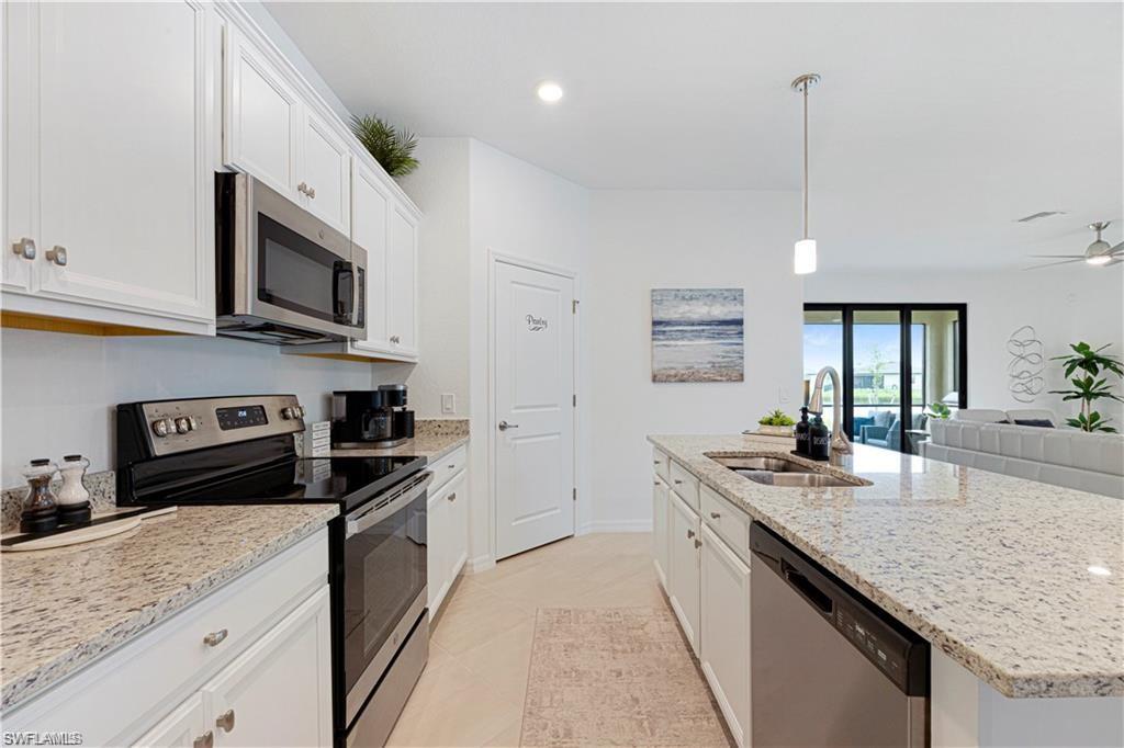 Kitchen featuring white cabinetry with silver hardware, granite countertops, stainless steel appliances, and a central island with a double basin sink
