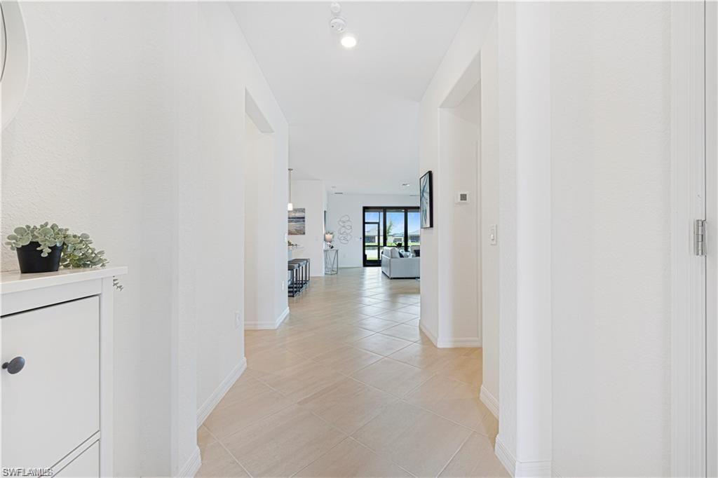 Bright hallway with light-toned tiled flooring, white painted walls, recessed ceiling lighting, and a white baseboard trim