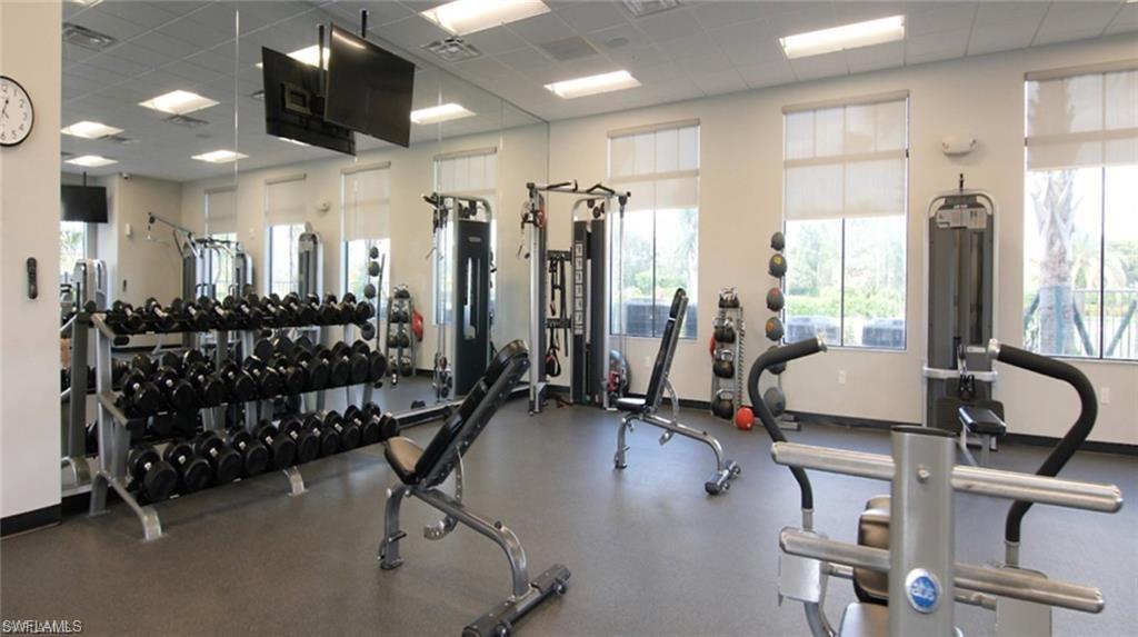Dedicated fitness center featuring rubber flooring, extensive mirrored walls, and large windows with privacy shades