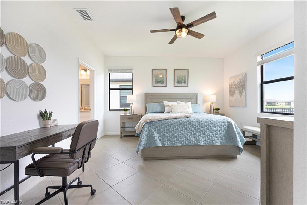 Spacious bedroom featuring light-toned tile flooring, a dark wood-finish ceiling fan, and multiple windows