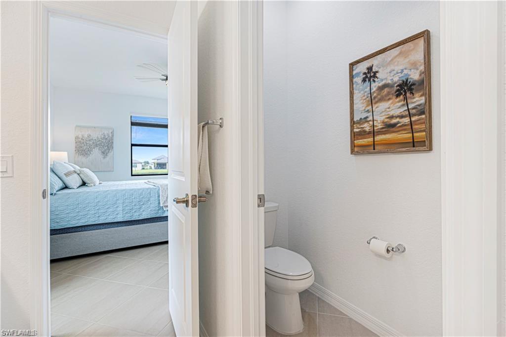White interior door with brushed nickel hardware, opening to a bright bedroom with light-colored tile flooring and a large window