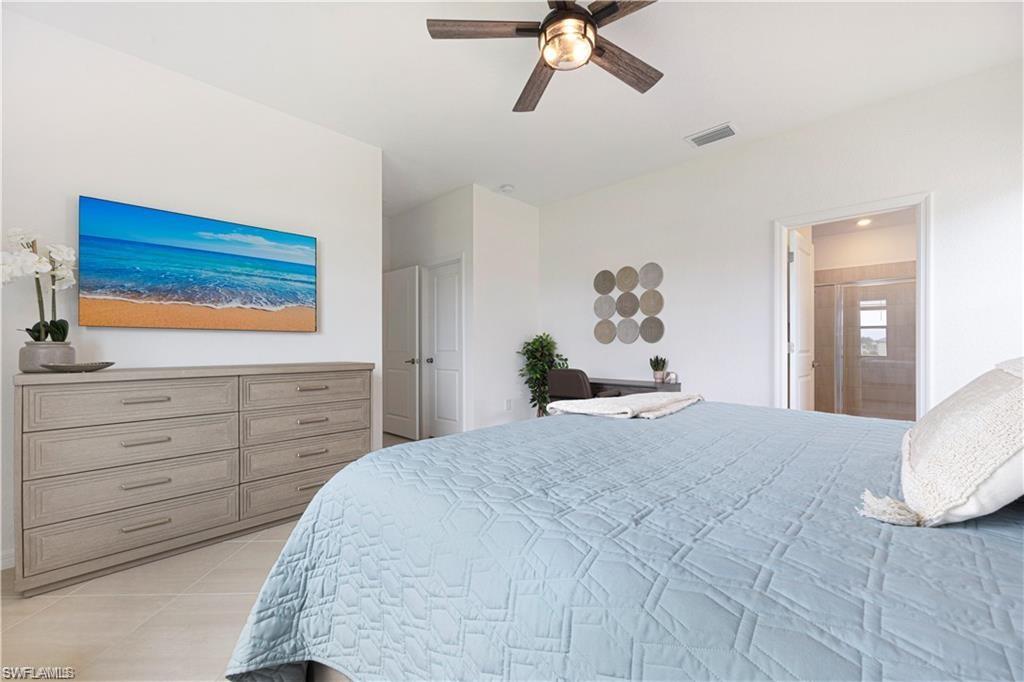 Spacious bedroom featuring light-toned flooring, a ceiling fan with integrated lighting, a recessed wall niche, and an entry to an interior space