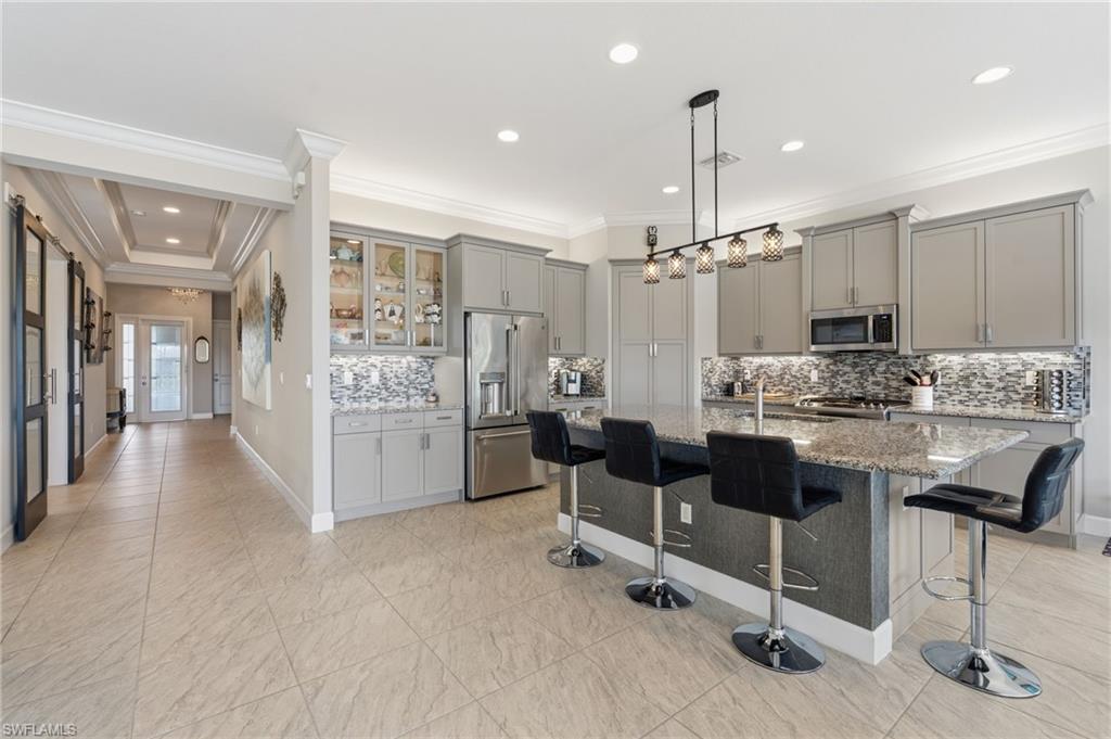 Stunning foyer entry and open kitchen with crown molding, gorgeous glass tile backsplash, glass cabinet door features, built-in pantry, high level cabinets with upper and under cabinet lighting.
