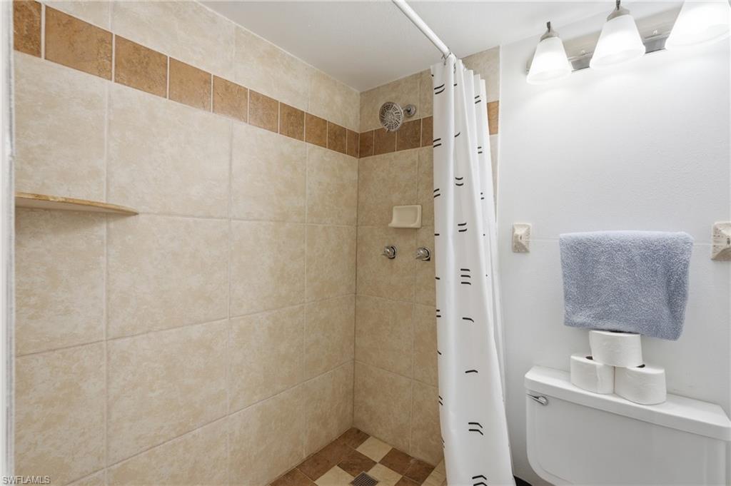 Tiled shower stall featuring an integrated corner shelf, a patterned floor, and a shower head with controls