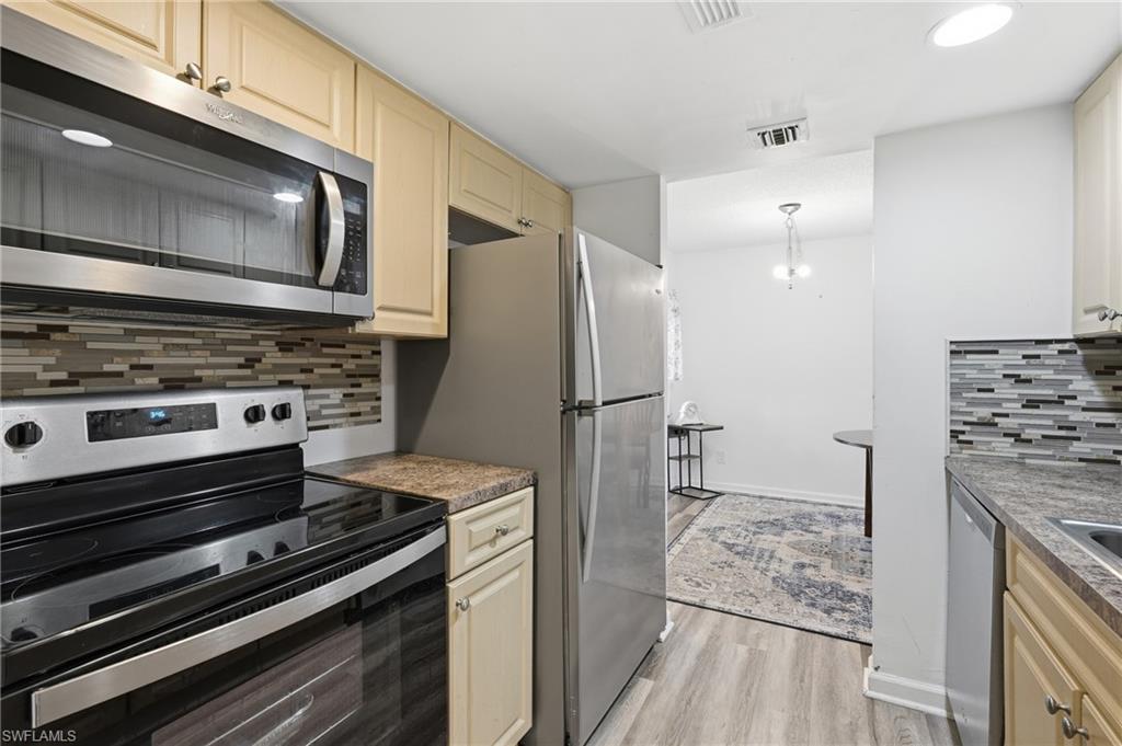 Kitchen featuring stainless steel appliances, light wood-finish cabinetry, and a mosaic tile backsplash
