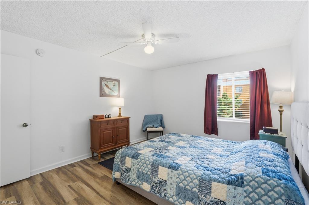 Primary Bedroom with wood-finish flooring, white walls, and a window featuring blinds and red curtains