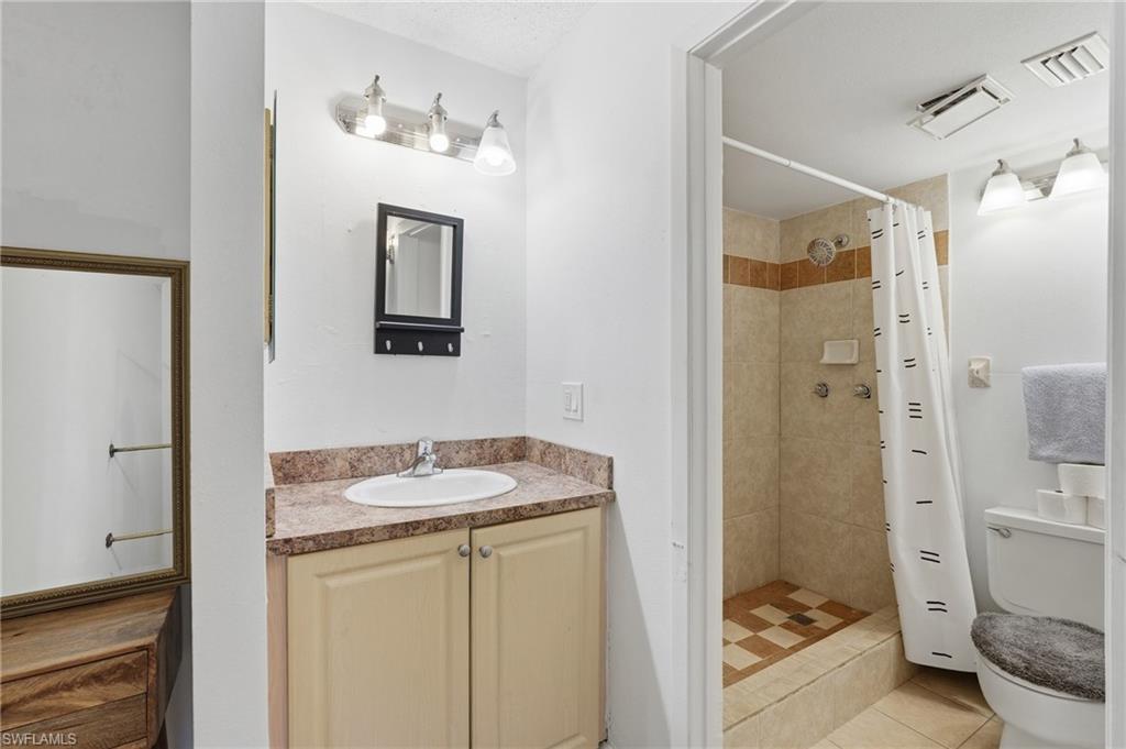 Full bathroom featuring a single vanity with a laminate countertop, light-toned cabinetry, and a walk-in shower with tile surround and a decorative accent band