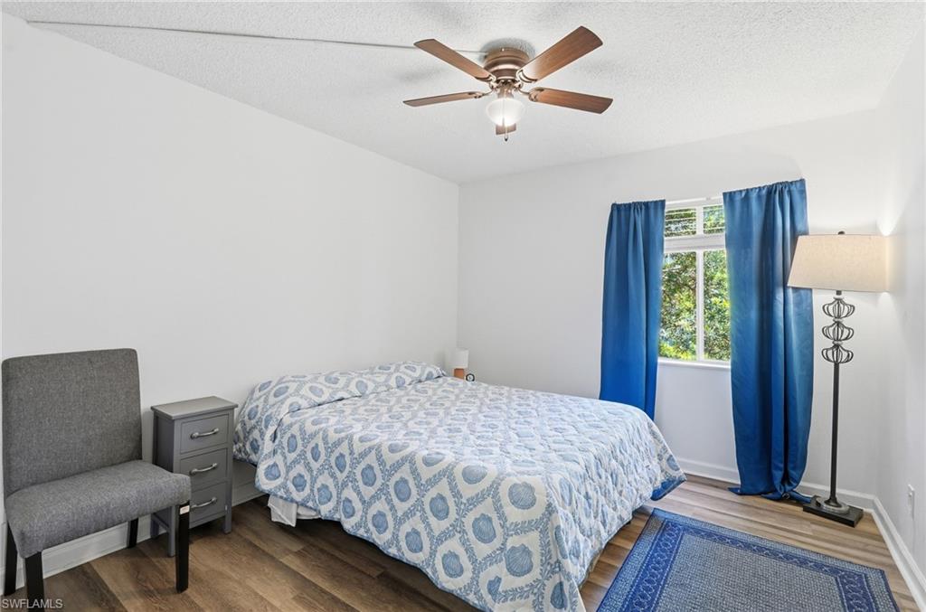 2nd Bedroom featuring a ceiling fan with integrated lighting, wood-finish flooring, a window with exterior tree foliage visible, white painted walls, and white baseboards