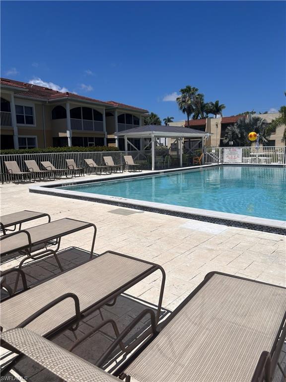 Outdoor swimming pool with a surrounding paved deck, white fencing, and an adjacent shaded gazebo