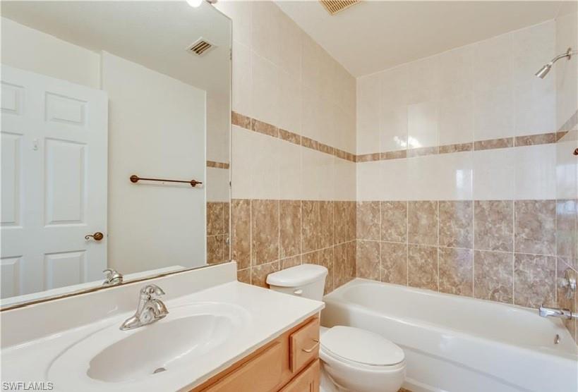 Bathroom featuring a light wood-finish vanity with an integrated sink, a full-width mirror, and a tiled shower-tub combination