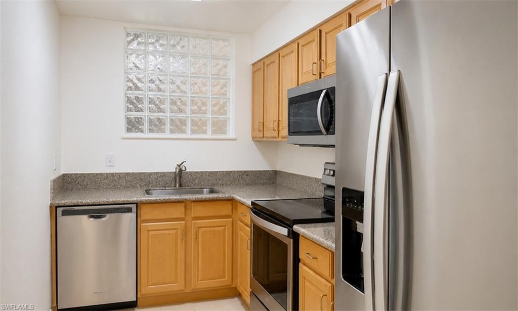 Kitchen featuring light wood cabinetry, stainless steel appliances, a glass block window, and a light-toned countertop