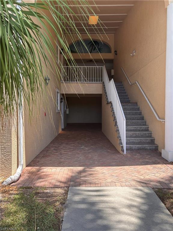 Entryway featuring a brick paver drive, concrete walkway, and exterior staircase with white railings
