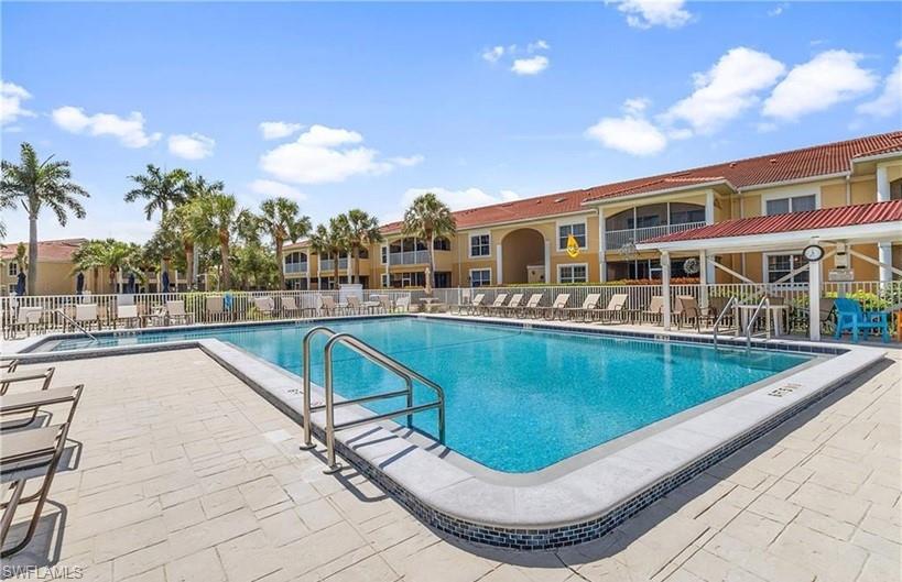 Community swimming pool with a mosaic tile border and integrated steps, surrounded by light-toned paver decking