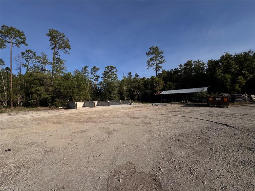 Expansive gravel lot surrounded by mature trees, featuring a large pole barn structure with a corrugated metal roof
