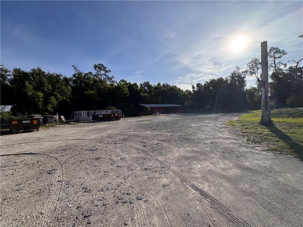 Expansive gravel lot with surrounding dense foliage and a red structure
