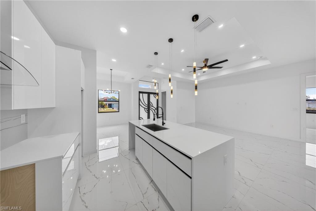 Modern kitchen featuring an extended island with a built-in sink and pendant lighting, white cabinetry, quartz countertops, and large format polished tile flooring